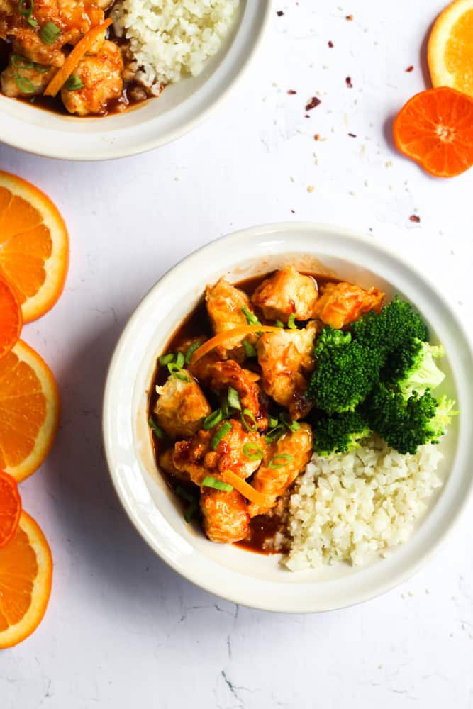 paleo orange chicken recipe with broccoli and cauliflower rice in a white bowl.