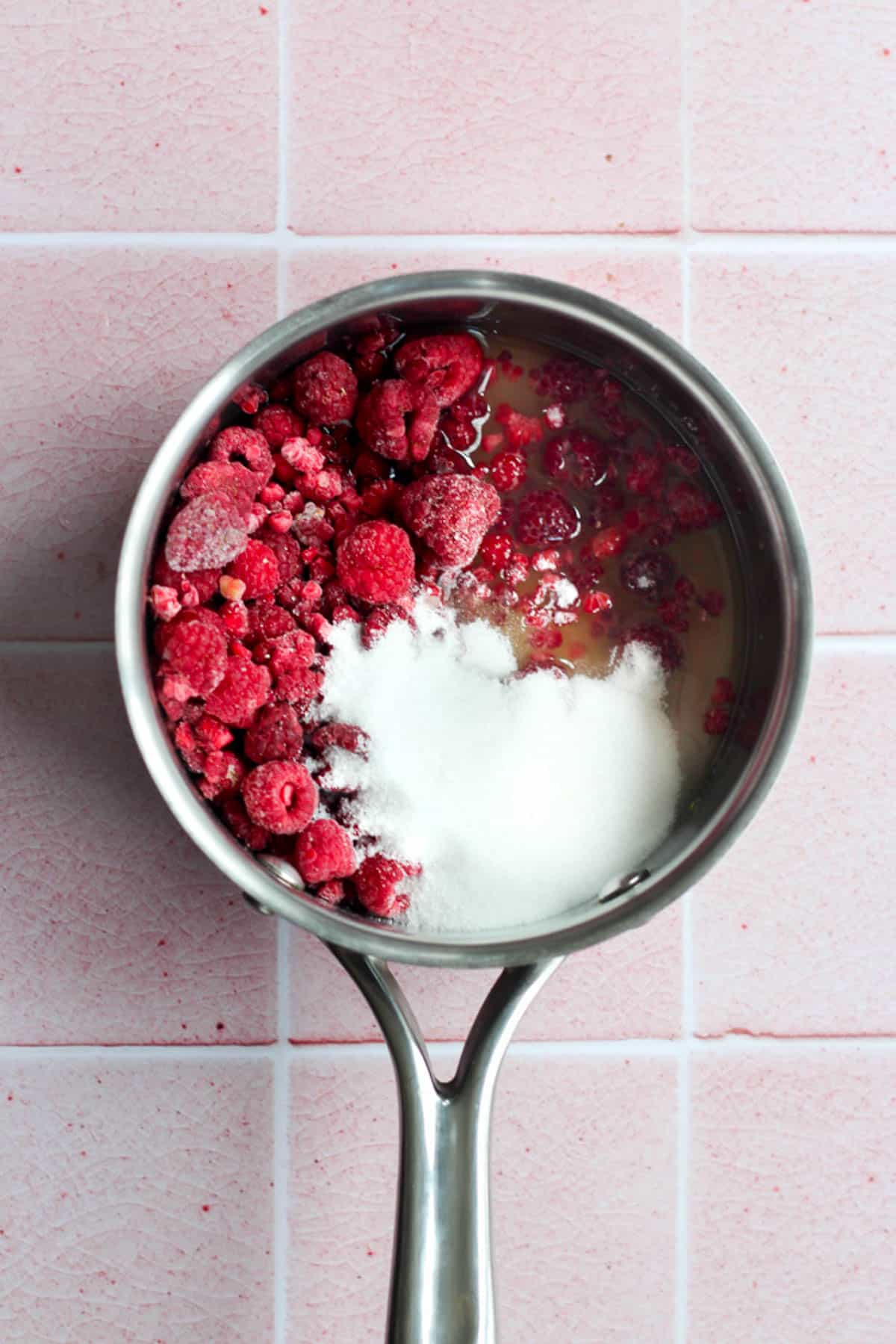 frozen raspberries, sugar, and juice in a silver pot.
