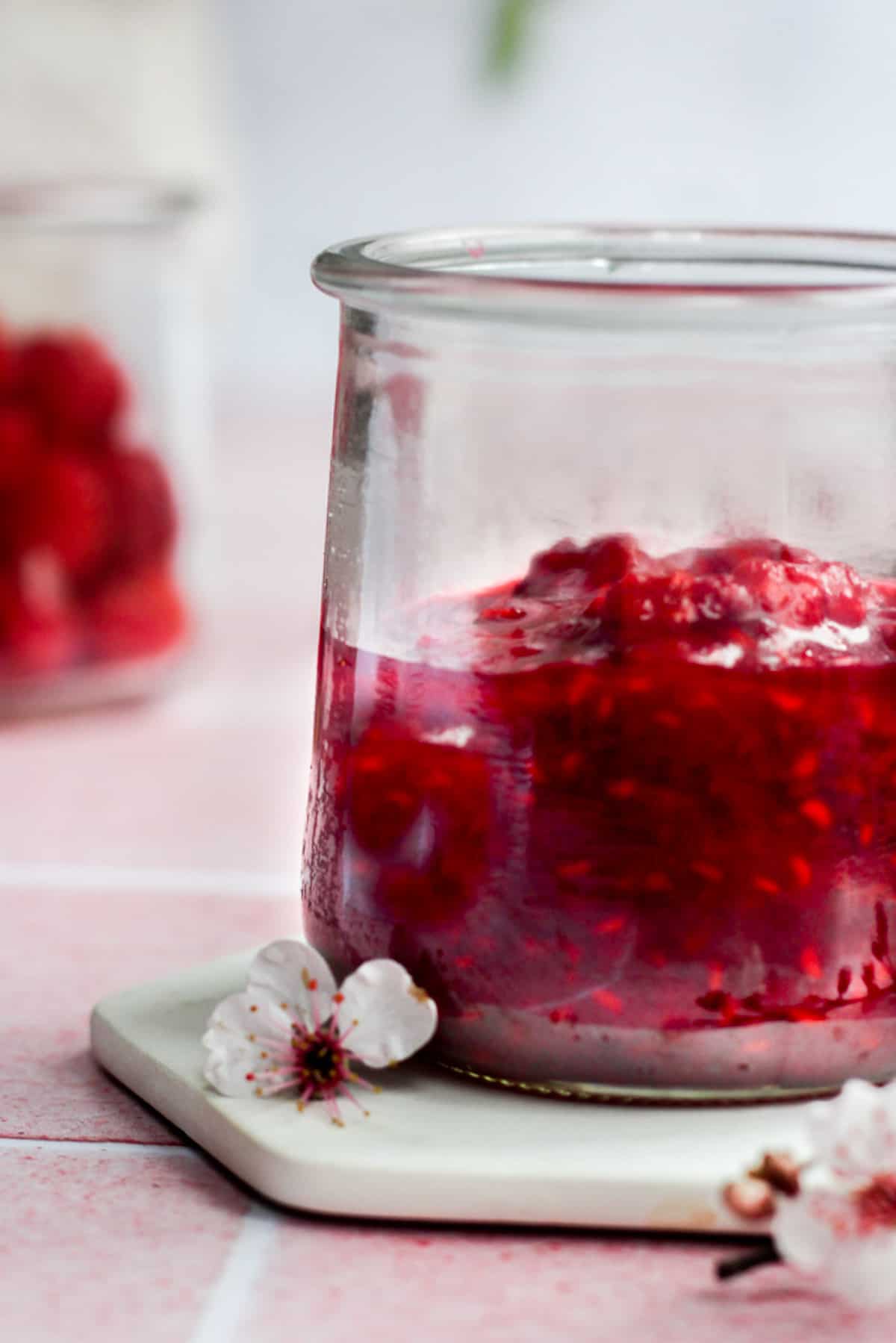 glass jar of raspberry compote on a white coaster.