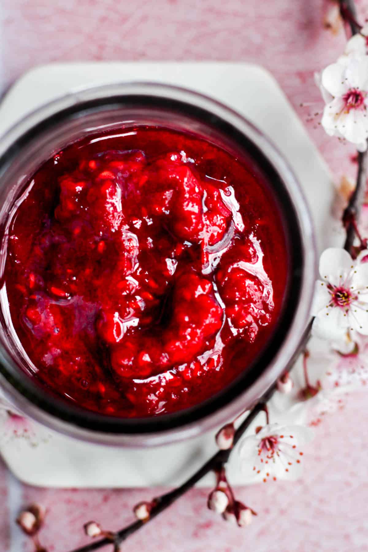 overhead view of raspberry compote in a glass jar.
