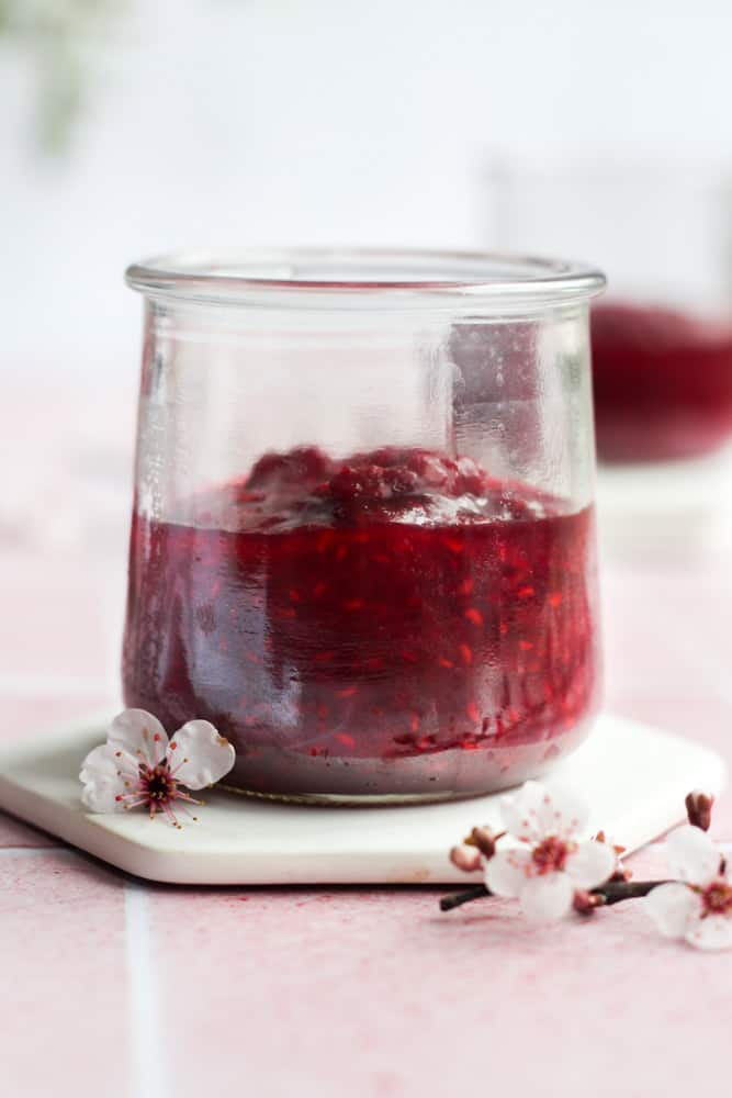healthy fruit sauce in a glass jar with red flowers.