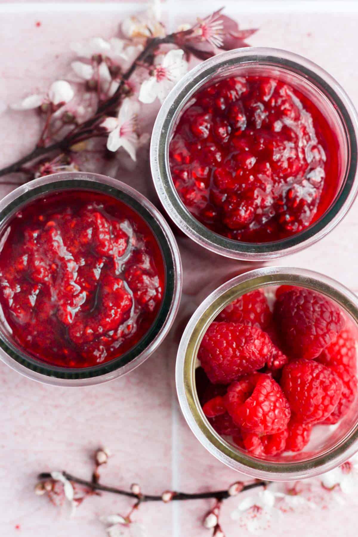 3 jars of raspberry compote on a pink backdrop.