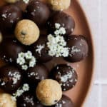 healthy cookie dough bites covered in chocolate on a tan plate with flowers.