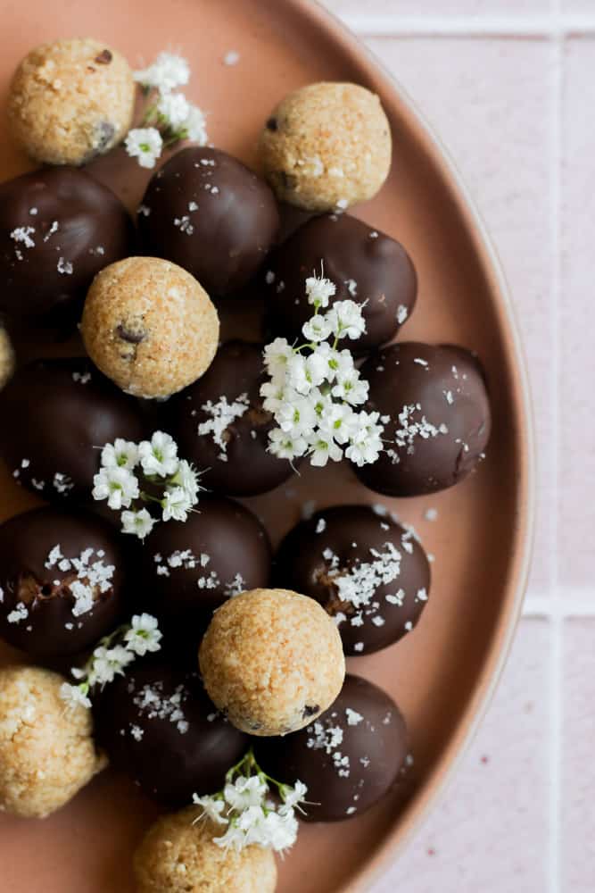 healthy cookie dough bites covered in chocolate on a tan plate with flowers.