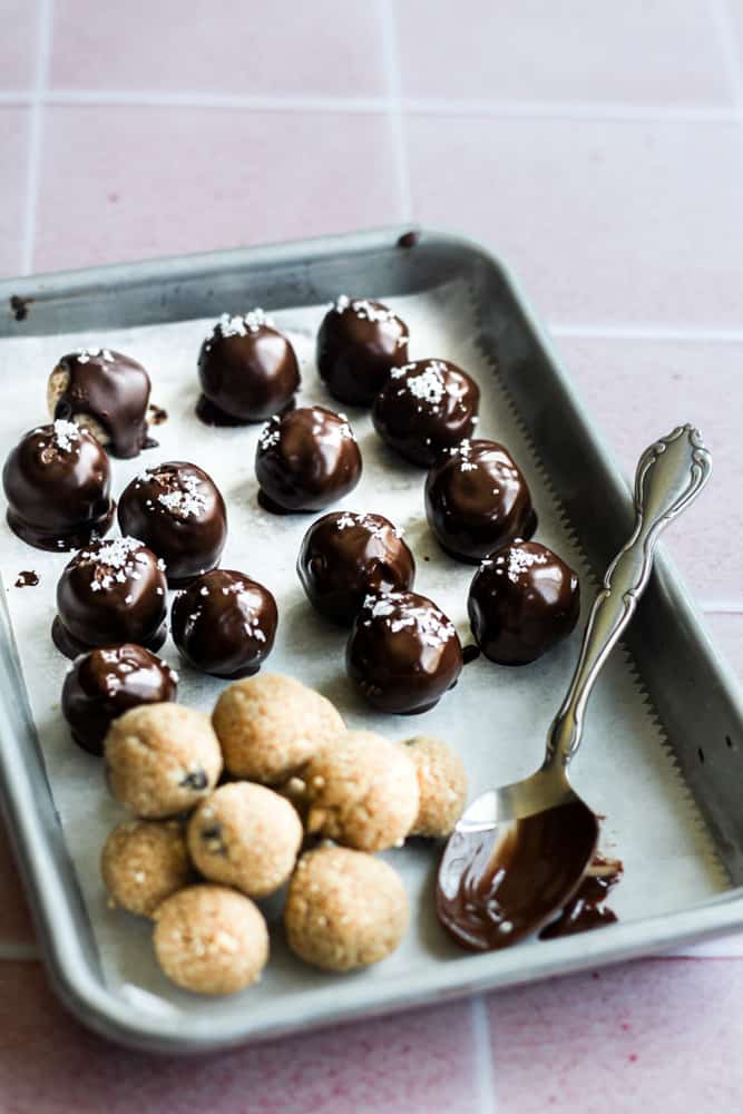 edible cookie dough bites coated in chocolate on a parchment lined baking sheet.