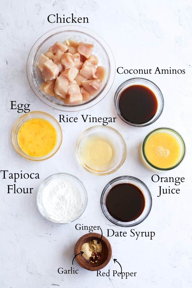 ingredients for paleo orange chicken on a white backdrop labeled with black text.