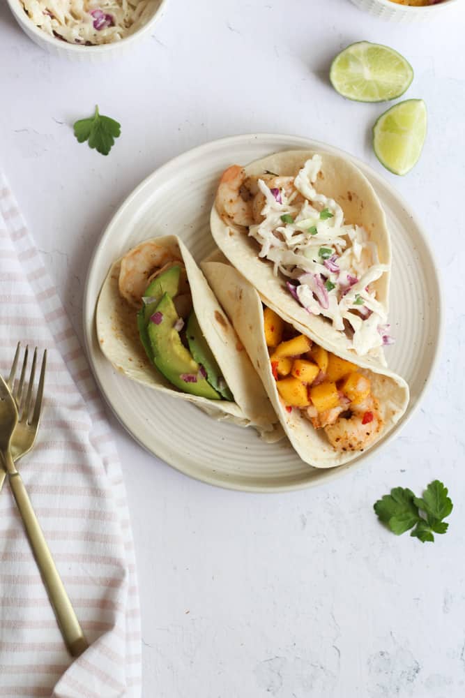 healthy shrimp tacos on a white plate toped with salsa and slaw.