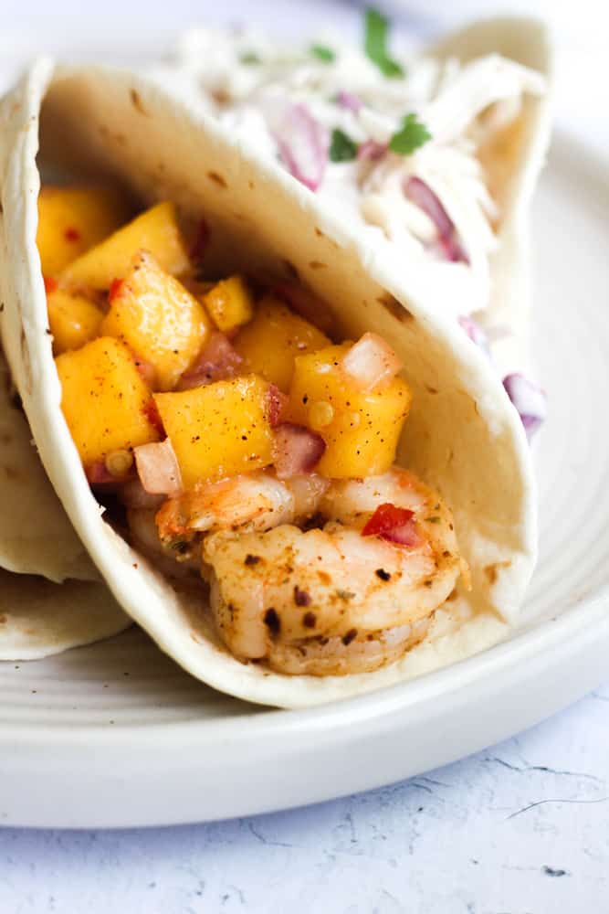 quick shrimp tacos topped with mango salsa on a white plate.