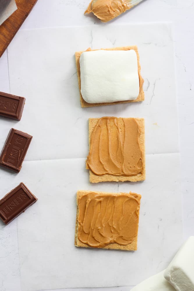 graham crackers with peanut butter spread on them and a marshmallow.