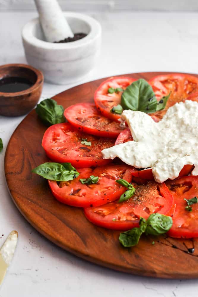 easy caprese salad with burrata on a wood platter with fresh basil and balsamic glaze.