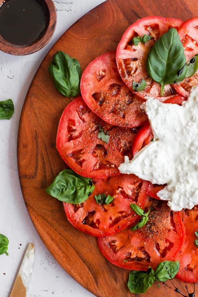 sliced tomatoes on a wood tray with basil and cut burrata cheese.