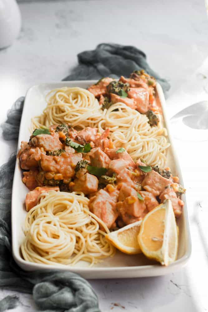 creamy chicken chipotle pasta with spaghetti and lemon wedges on a white platter.