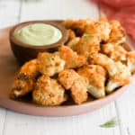 crispy cauliflower bites on a tan plate with an avocado dipping sauce in a bowl.