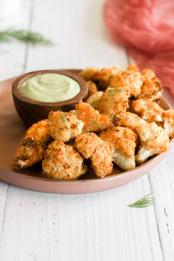 crispy cauliflower bites on a tan plate with an avocado dipping sauce in a bowl.