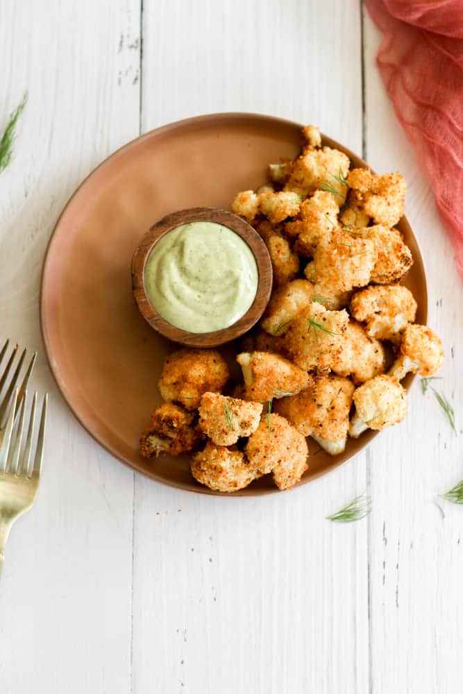 healthy air fried cauliflower on a tan plate with a green dipping sauce.