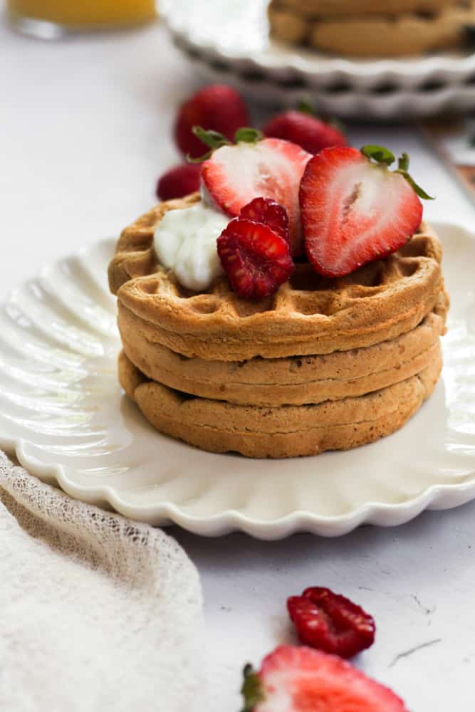 oat flour waffles topped with berries and yogurt on a white plate.