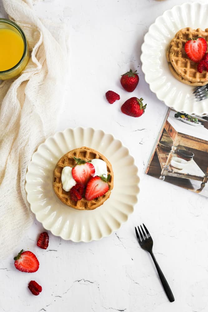oat flour waffles on white plates topped with berries.