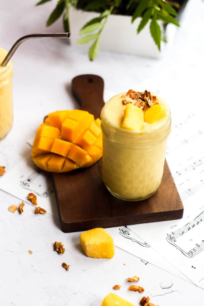 healthy pineapple mango smoothie on a wood board with cut mango.