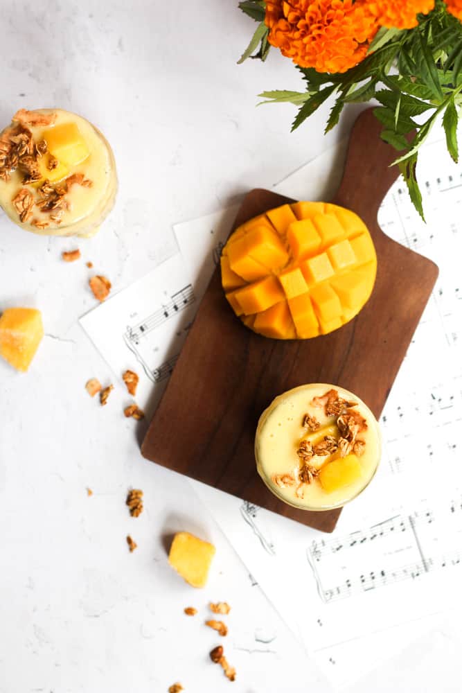 pineapple mango smoothie in glasses topped with granola and fresh mango.