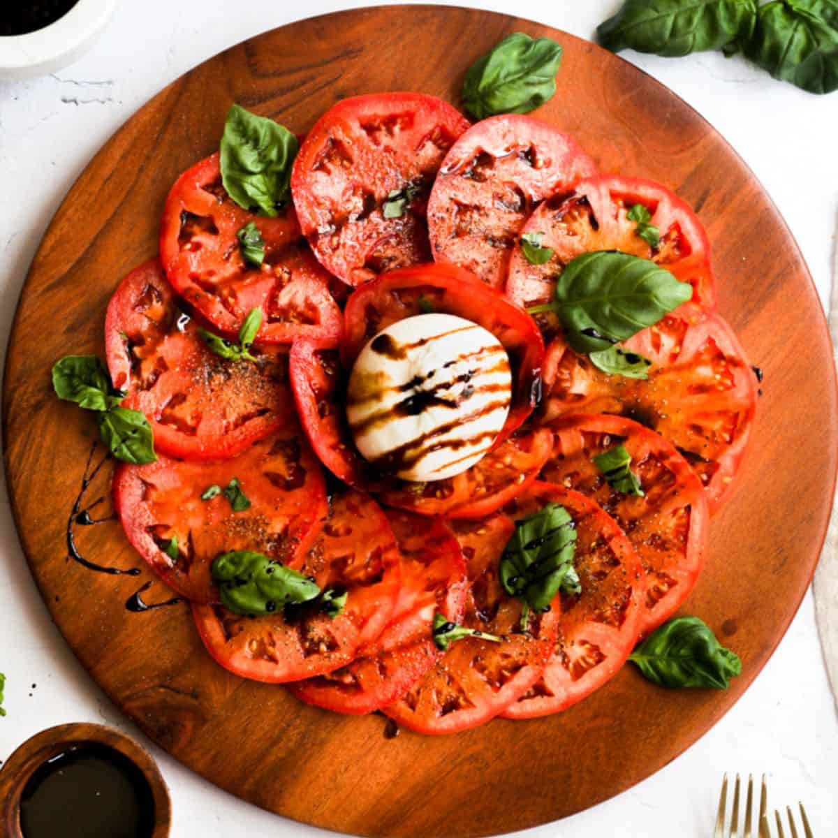burrata caprese salad on a wooden platter with fresh basil and a drizzle of balsamic.