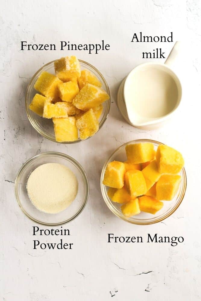 ingredients for a protein mango smoothie on a white backdrop labeled with black text.