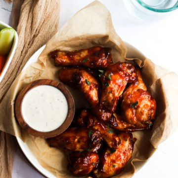 air fryer BBQ chicken wings in a bowl with brown parchment paper and a white sauce.