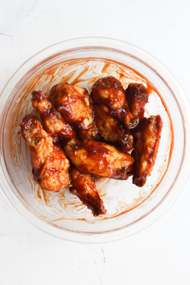 wings cooked in the air fryer tossed in BBQ sauce in a glass bowl.