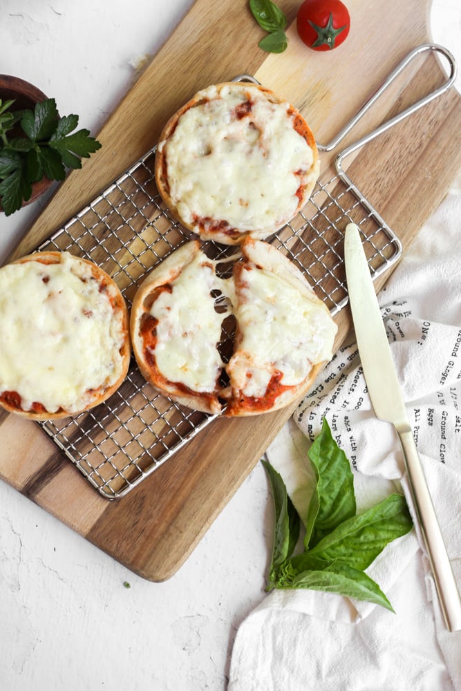 air fryer English muffin pizzas on a wire rack with 1 cut in half.