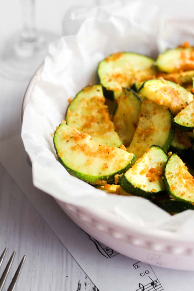 healthy crispy zucchini cooked in the air fryer on parchment paper in a pink bowl.