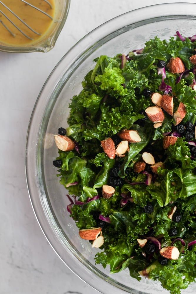 chick fil a kale salad in a clear bowl topped with chopped almonds.