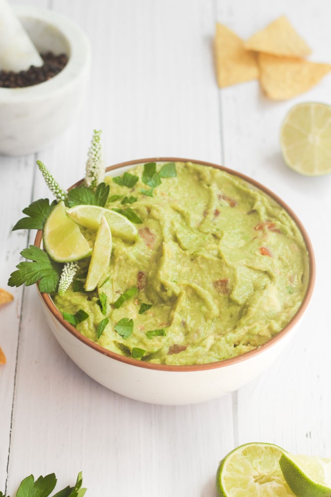 white bowl of healthy guacamole with lime slices and herbs.