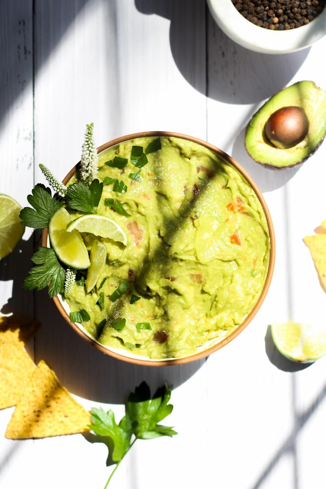 guacamole recipe with no onion in a white bowl with window pane shadows crossing over the center.