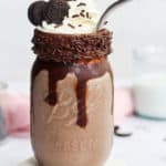 oreo milkshake without ice cream in a mason jar with whipped cream, sprinkles, and a straw.