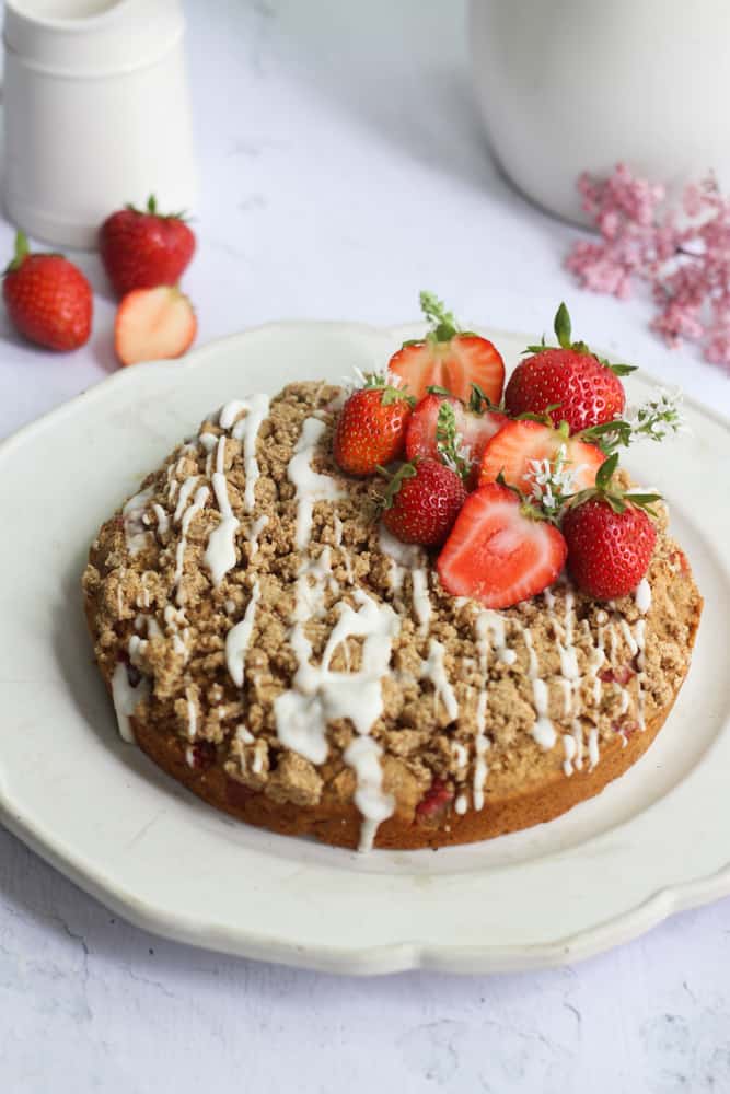 healthy strawberry banana cake with glaze and fresh strawberries on a white plate.