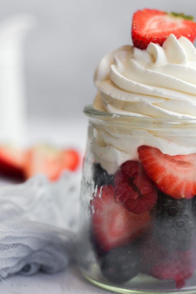 sugar free whipped cream piped in a glass jar of fresh fruit.