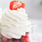 whipped cream without sugar in a jar of berries topped with a halved strawberry.