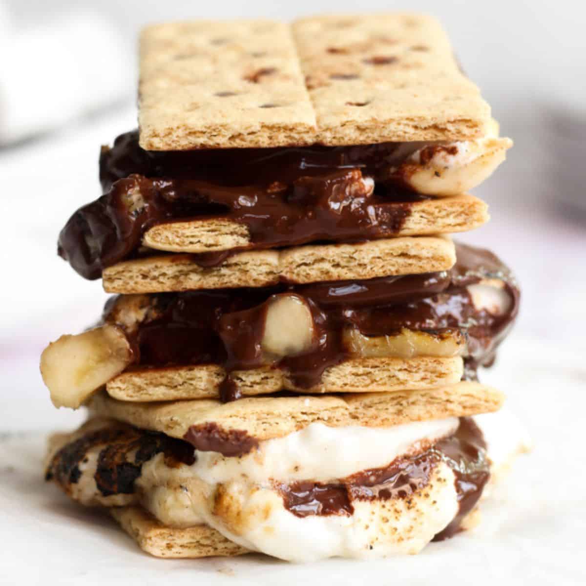 3 air fryer smores stacked on parchment paper with melted chocolate and marshmallows.