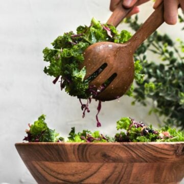 chick fil a kale salad in a wood bowl being served with wooden tongs.