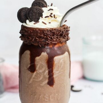 oreo milkshake without ice cream in a mason jar with whipped cream, sprinkles, and a straw.