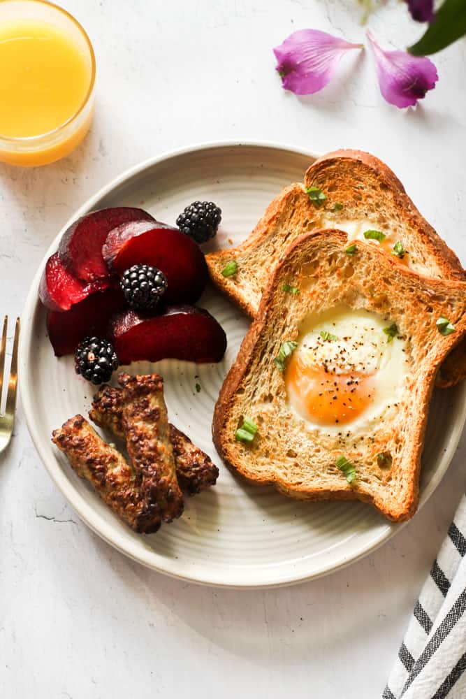 air fryer egg in a hole on a white plate with sausage and fruit.