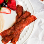 turkey bacon in air fryer on white plate with strawberries.