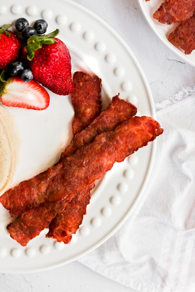turkey bacon in air fryer on white plate with strawberries.