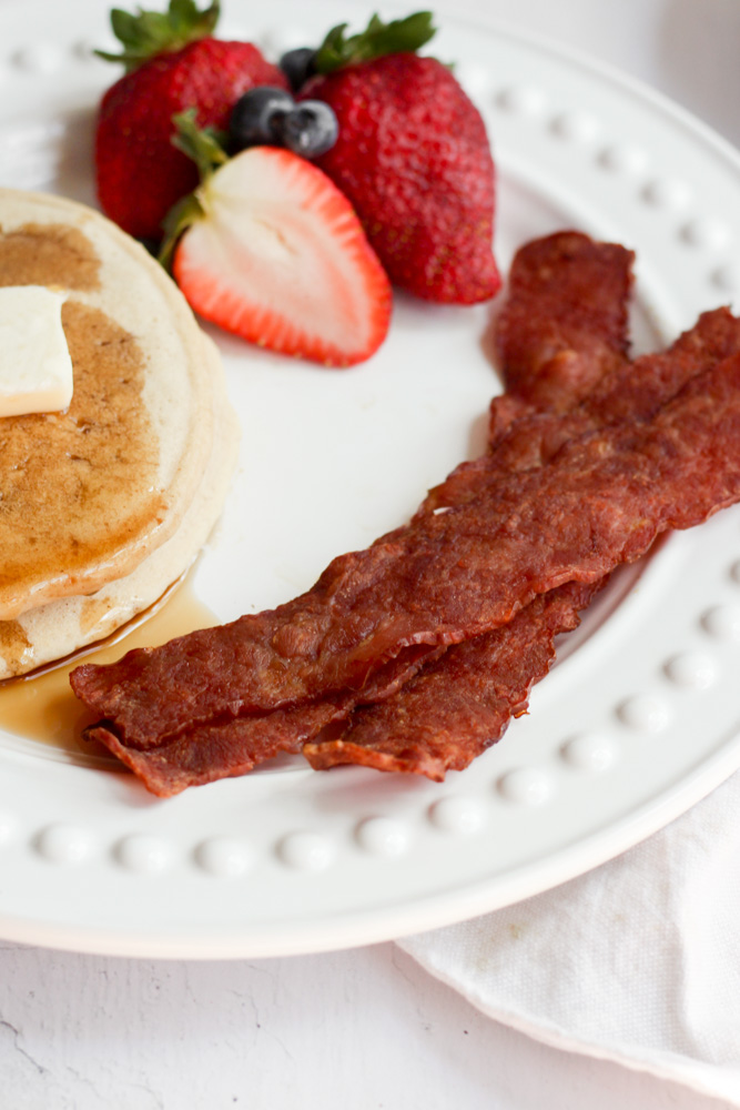 air fryer bacon on white plate with pancakes and fruit.