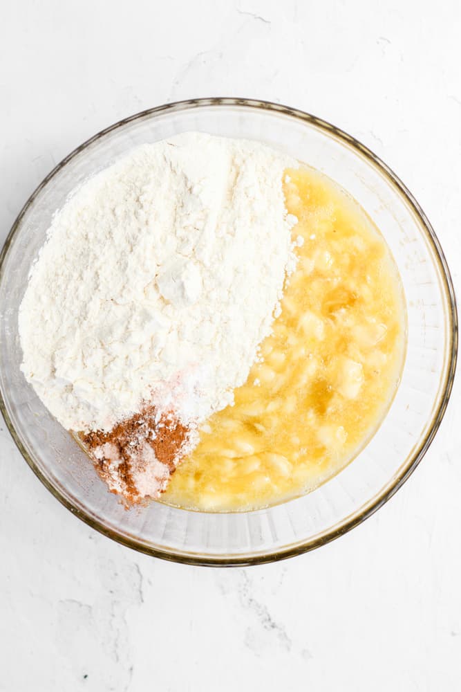 dry ingredients added to a bowl of mashed bananas.