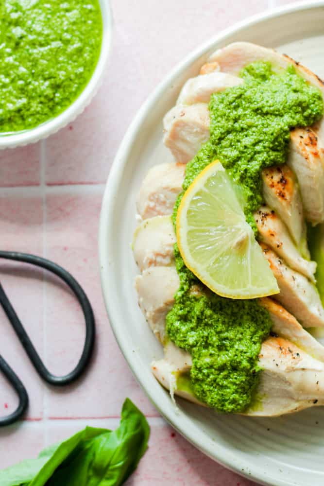 grilled chicken on a white plate topped with nut free pesto.