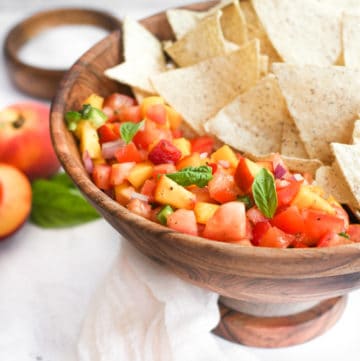peach mango salsa in a wood bowl with tortilla chips.