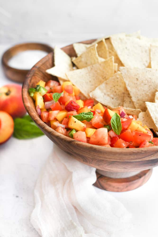 peach mango salsa in a wood bowl with tortilla chips.