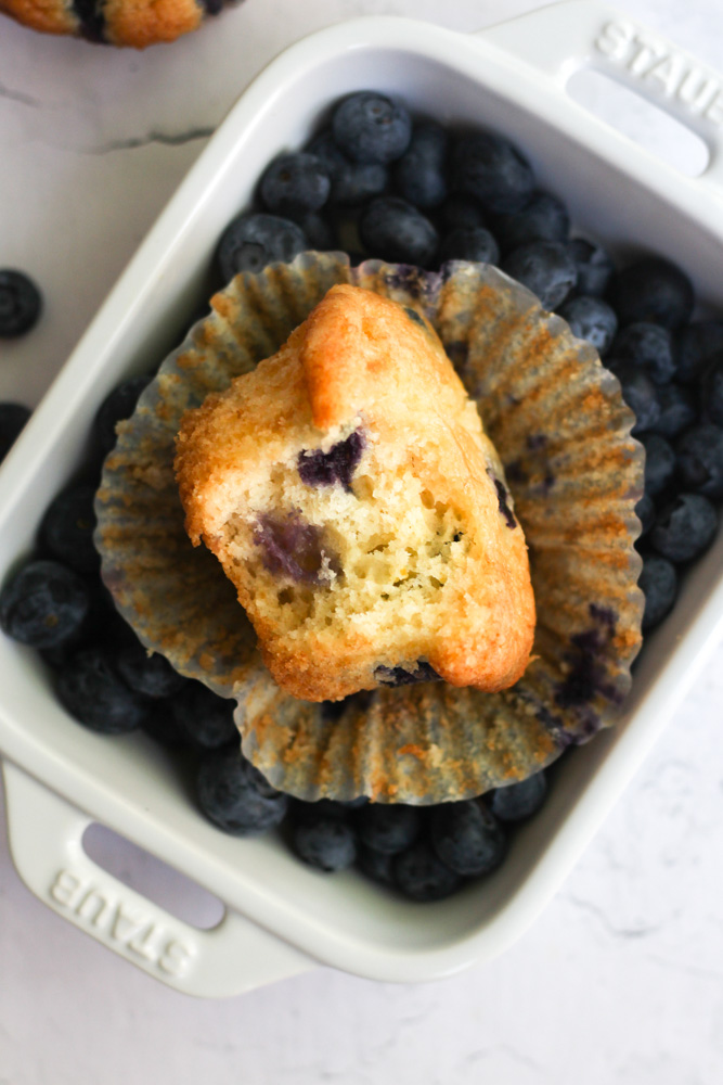 blueberry muffin with a peeled liner in a tray of fresh blueberries.