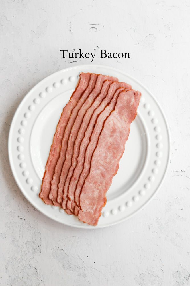 raw turkey bacon on a white plate with black text reading, "turkey bacon."