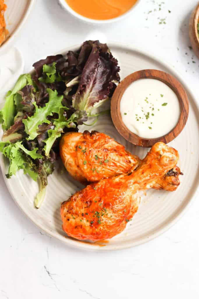 buffalo chicken legs on white plate with salad.